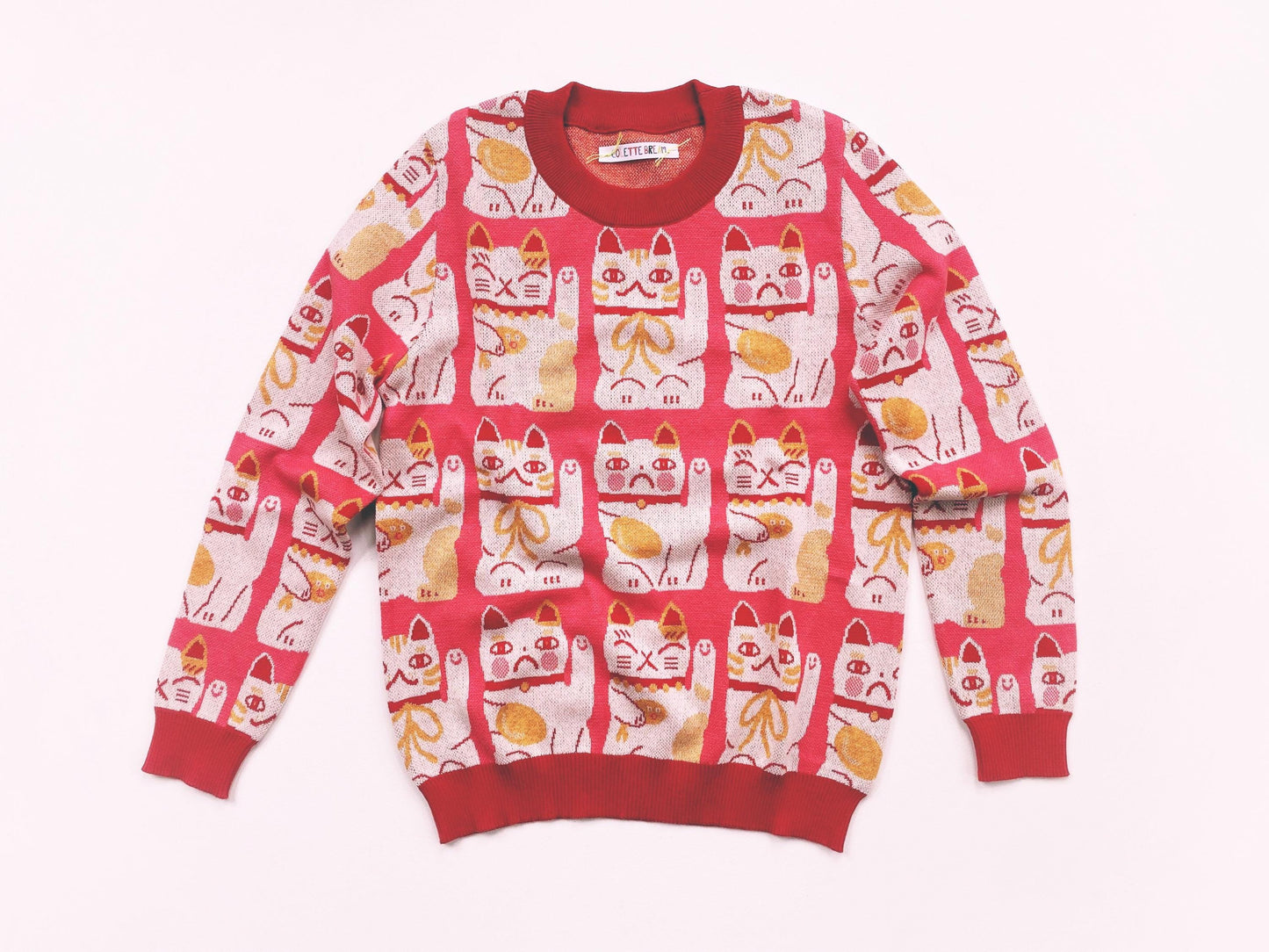 Red and pink sweater with maneki neko cat pattern on a white background