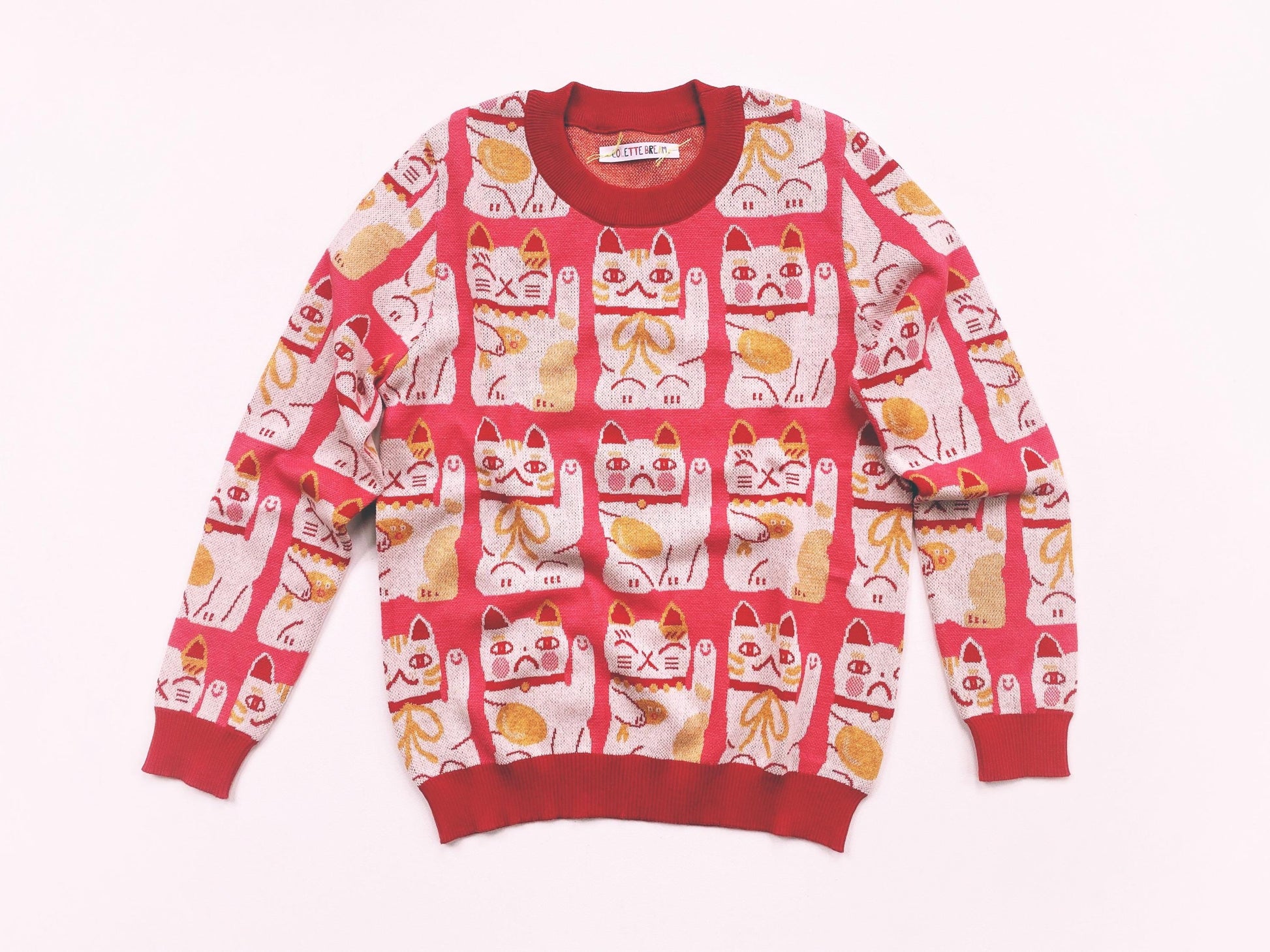 Red and pink sweater with maneki neko cat pattern on a white background