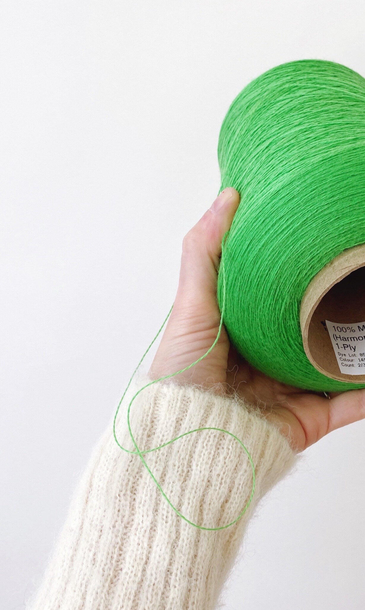 Hand holding a green spool of yarn against a white background