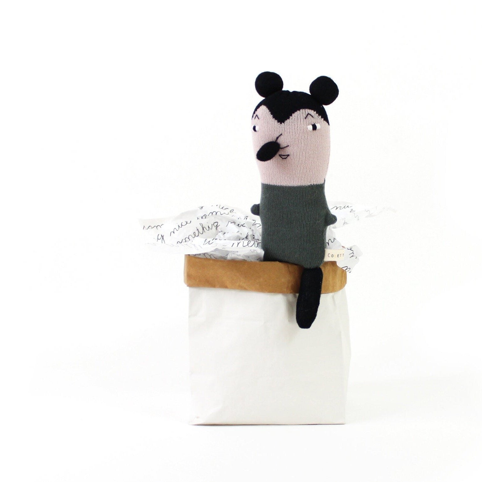 Knitted plush toy mouse with black ears and pink face sitting on a white box with a white background