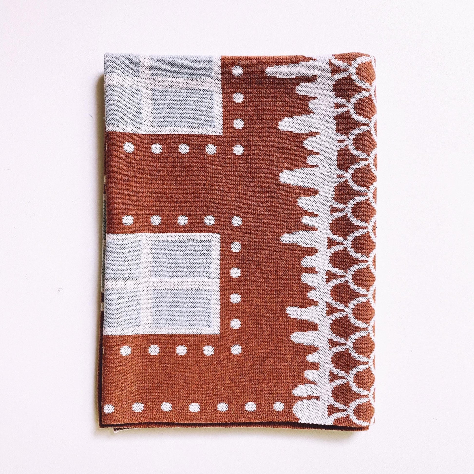 Detail of folded knitted blanket with brown, white, and gray pattern on a white background