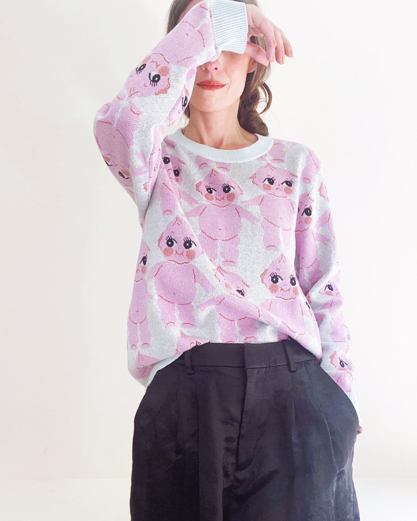 Person wearing a sweater with pink kewpie doll pattern on a white background