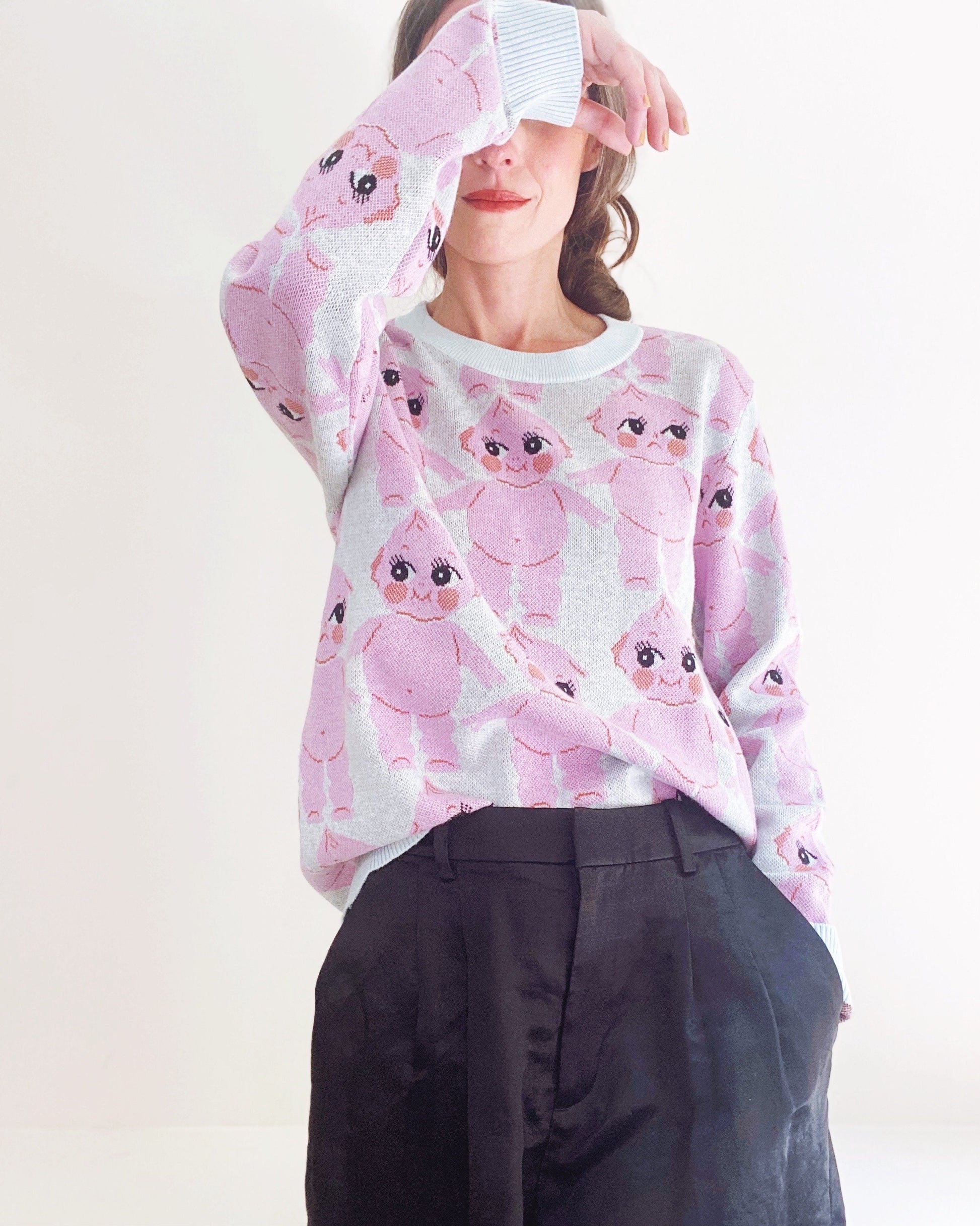 Person wearing a sweater with pink kewpie doll pattern on a white background