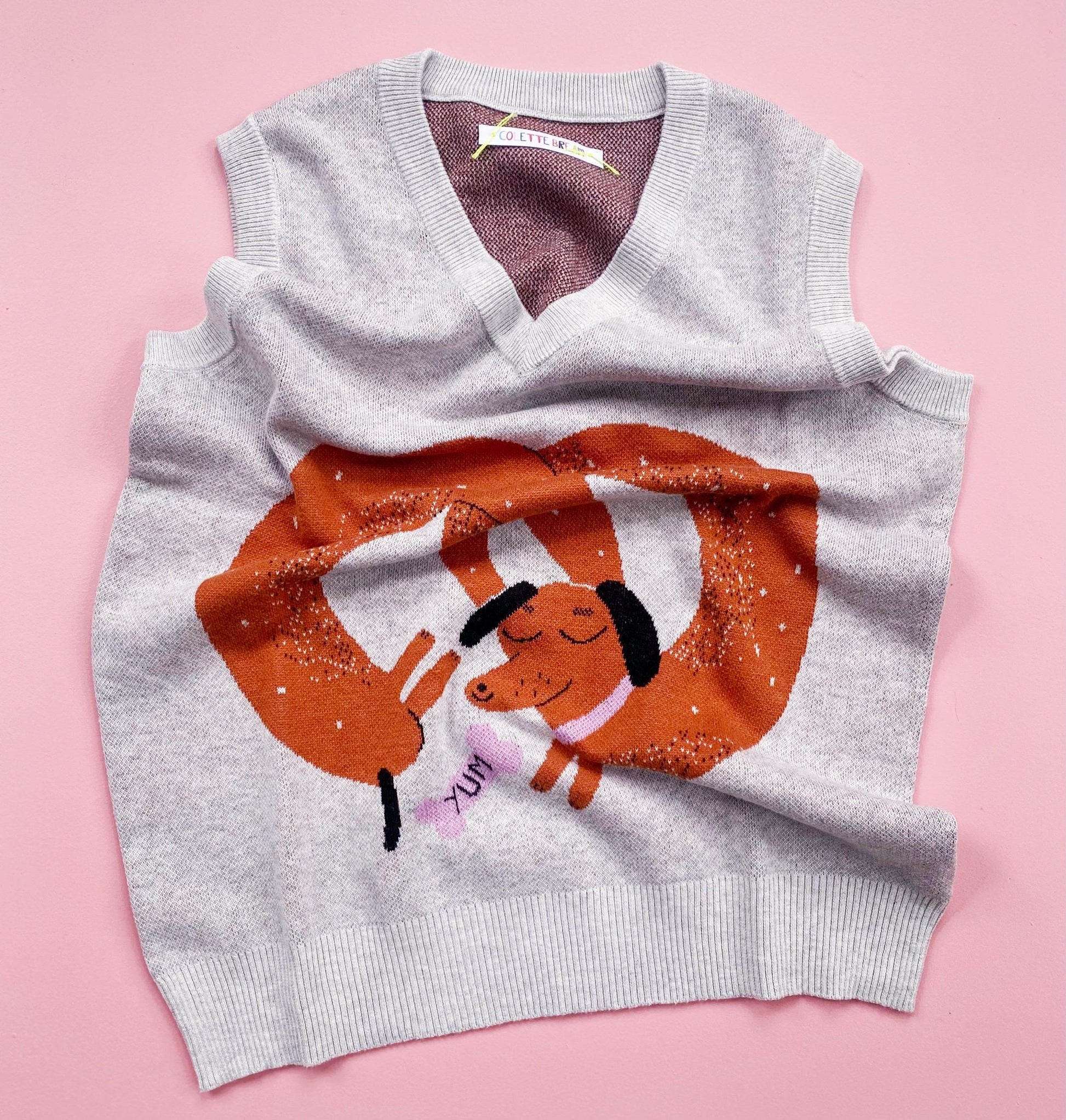 Gray sleeveless sweater with cartoon sausage dog design on a pink background