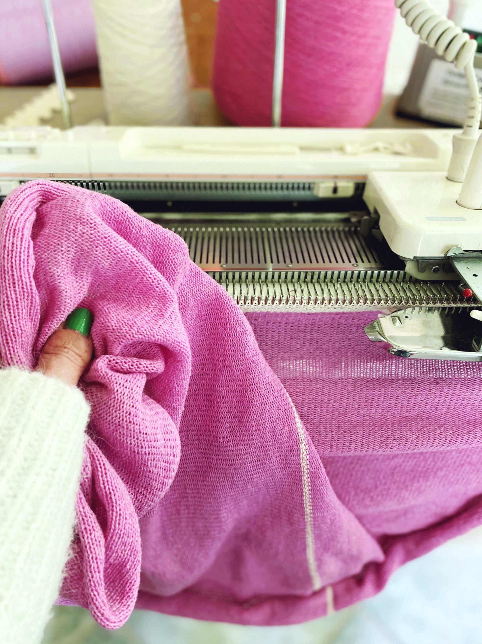 Person holding pink knitted fabric next to a knitting machine.