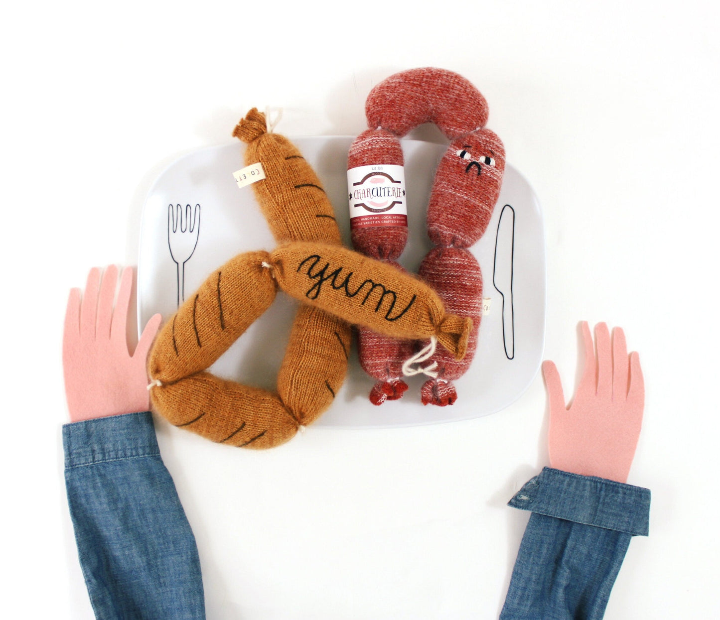 Two knitted plush toy sausages with a hand holding them on a white background
