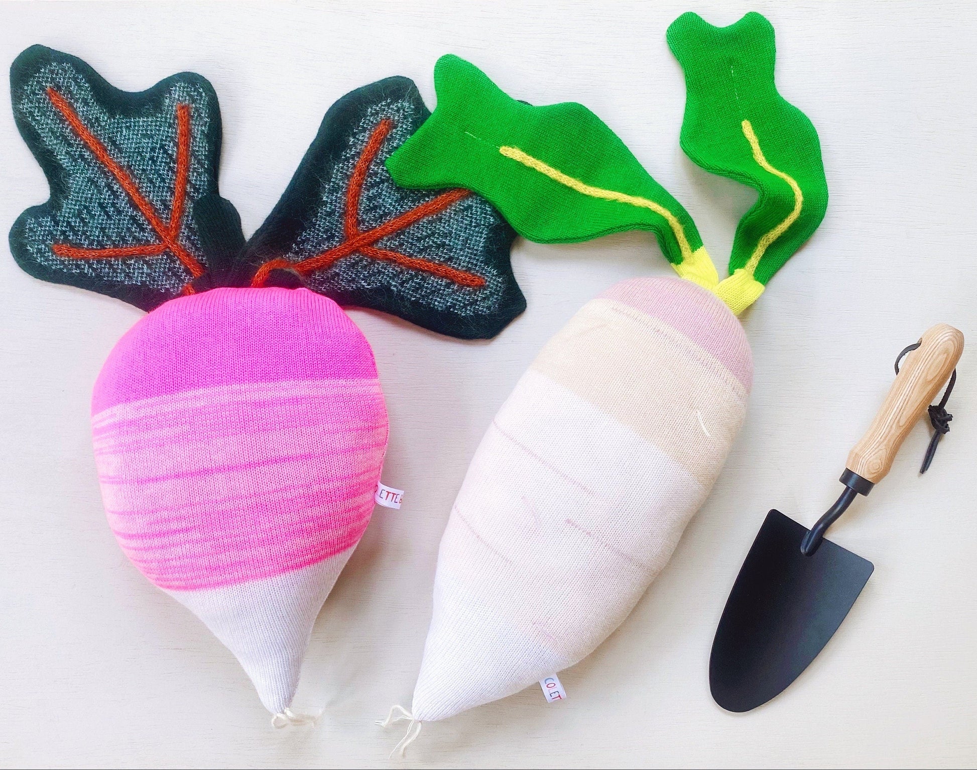 Toy radishes and turnip pillows with leafy tops and a small trowel on a light background