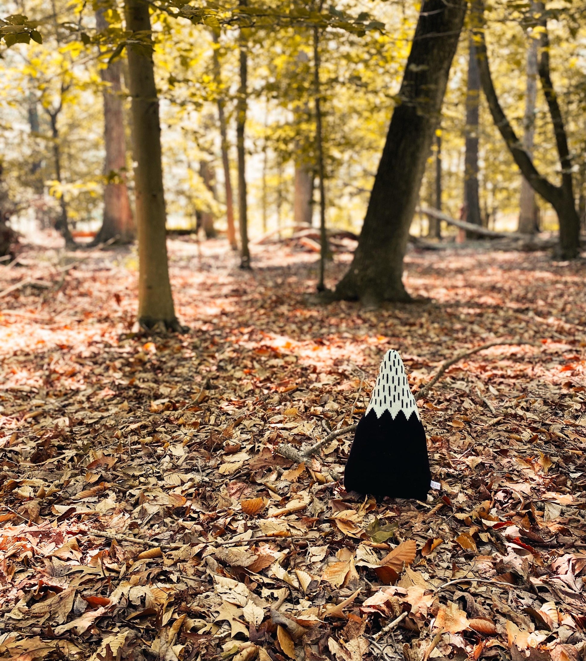 Black and white patterned mountain-shaped pillow on a forest floor with trees and fallen leaves.