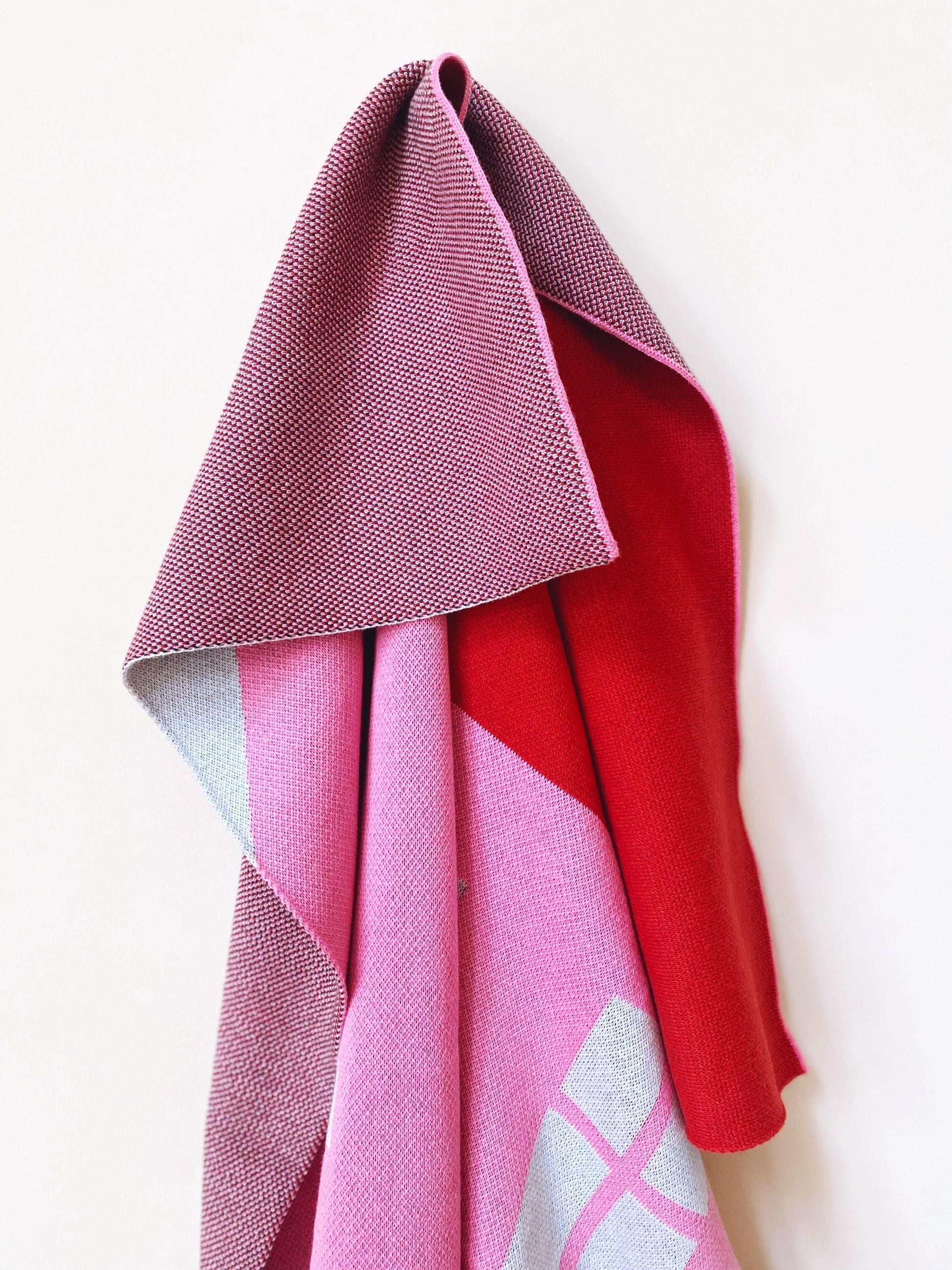 Folded pink and red knitted blanket on a white background