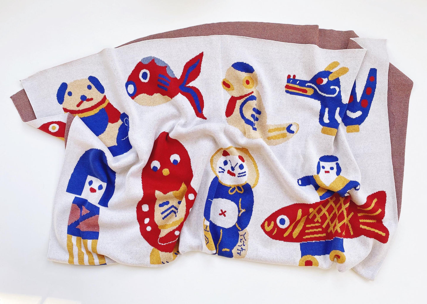 Folded knitted blanket with colorful cartoon-like japanese animal designs on a white background