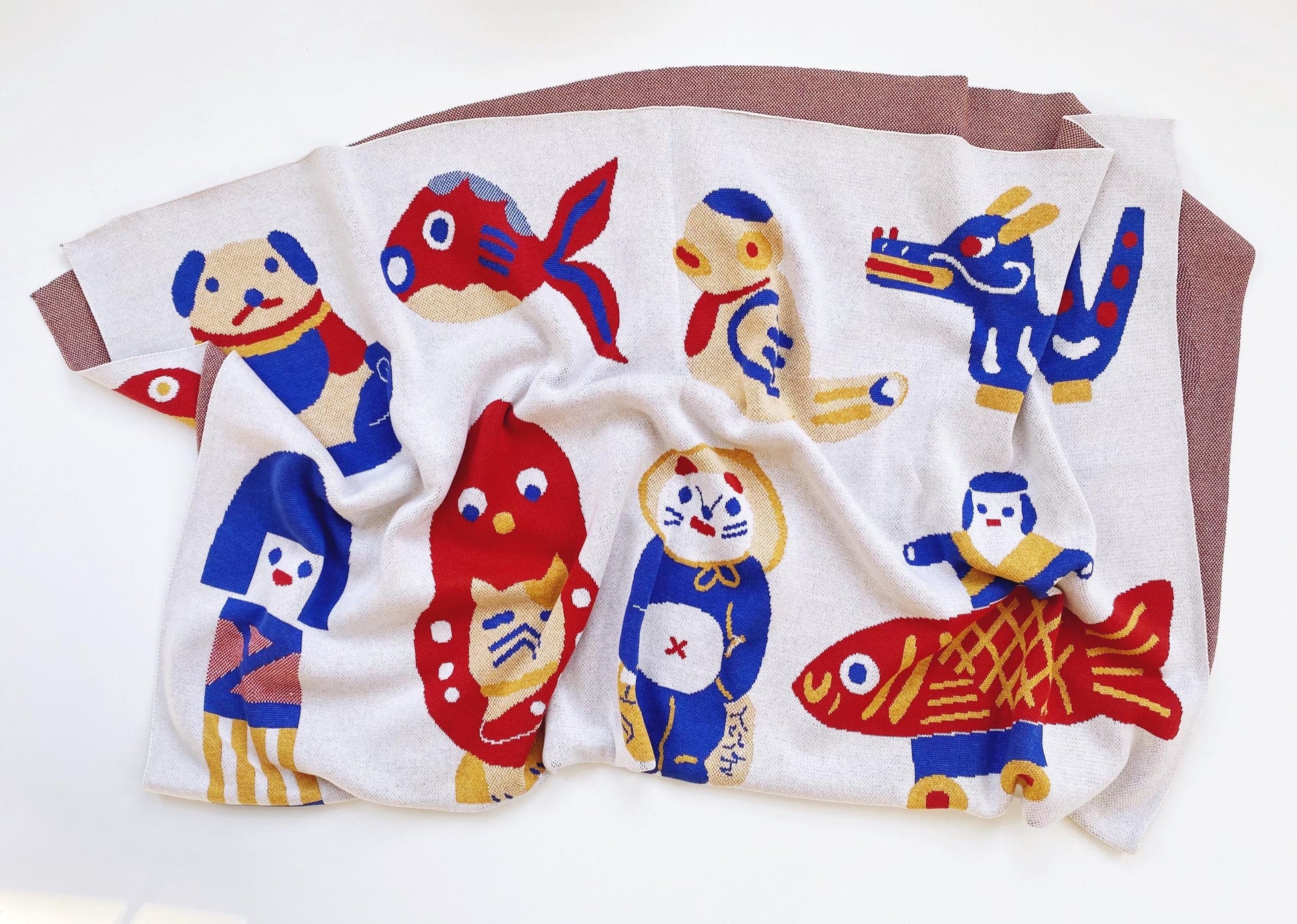 Folded knitted blanket with colorful cartoon-like japanese animal designs on a white background