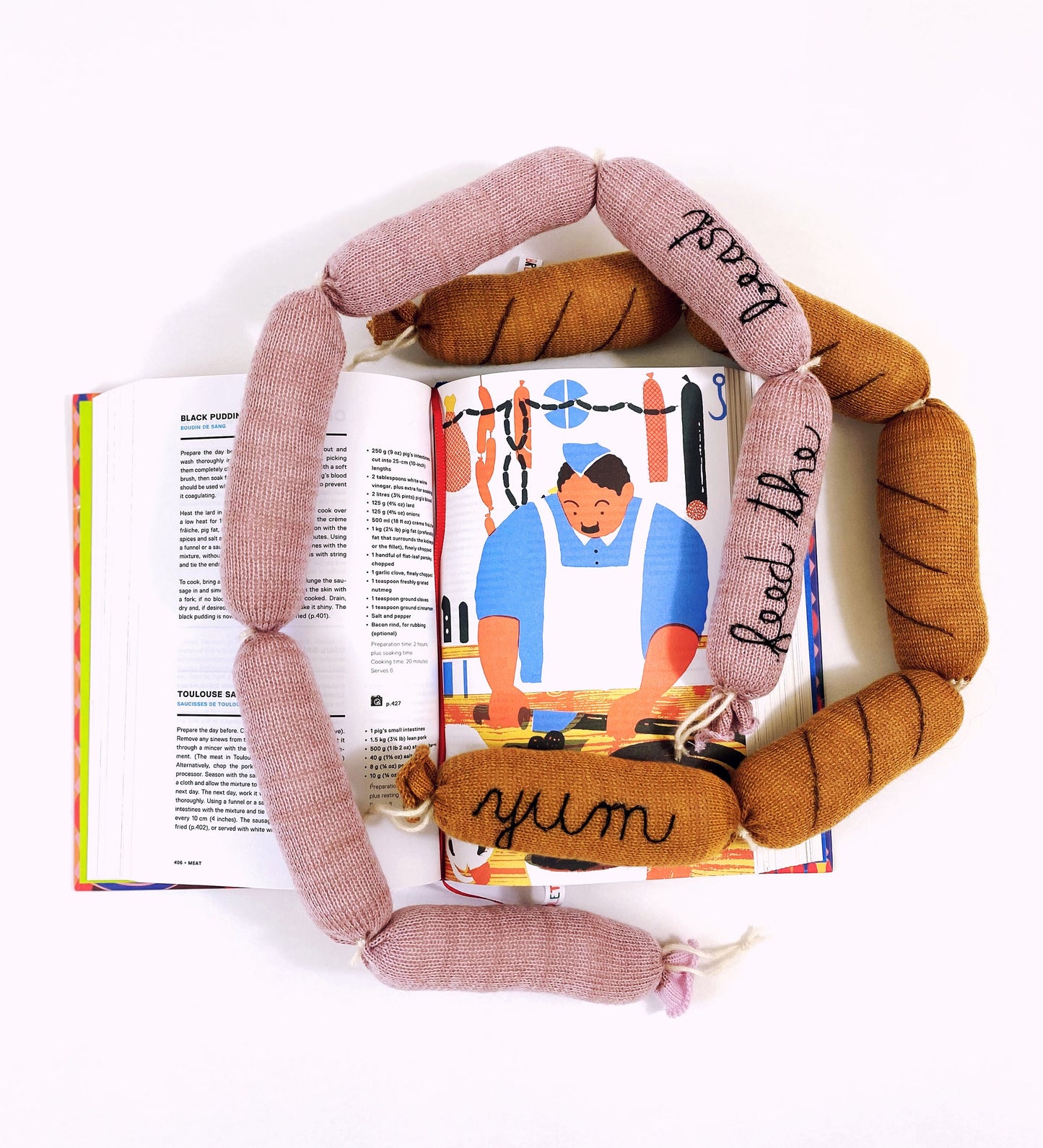 Textured pink and brown knitted sausage links with 'yum' on an open book