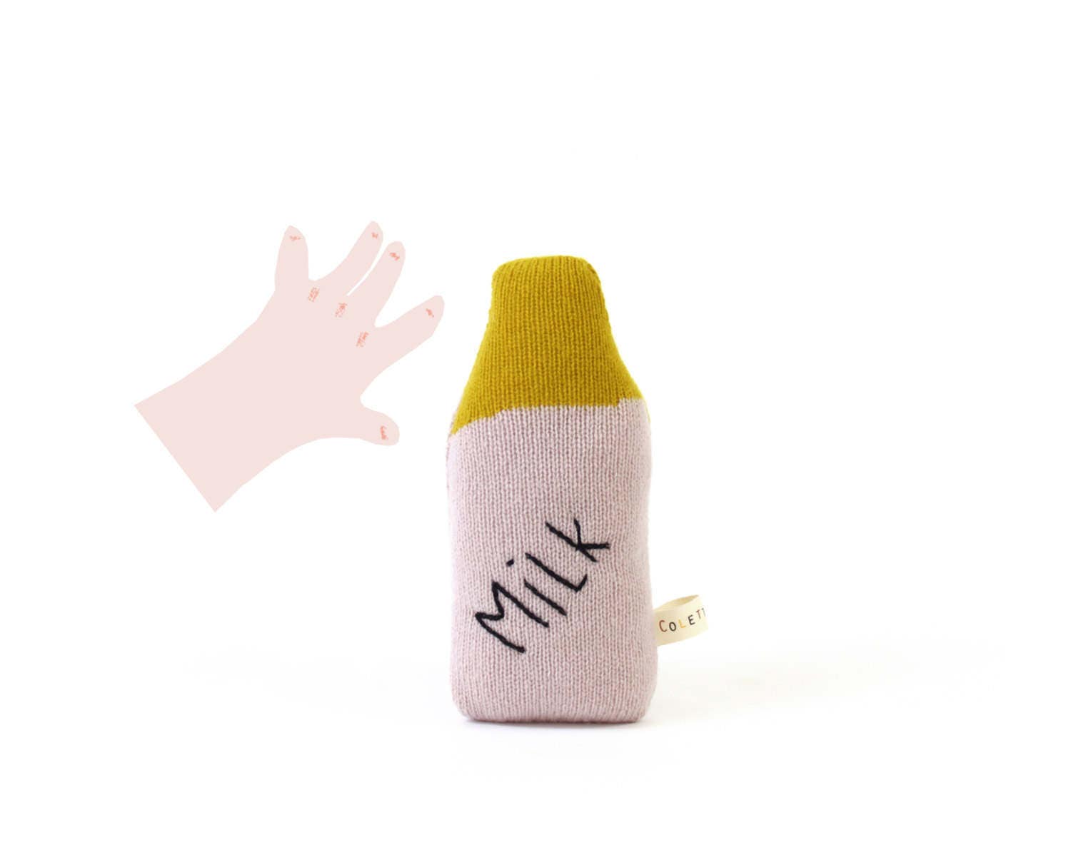 Knitted baby rattle shaped like a milk bottle with yellow top and pink body labeled 'Milk', next to a small pink hand toy, on a white background.
