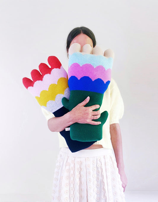 Person holding a colorful knitted flower-shaped pillows against a white background