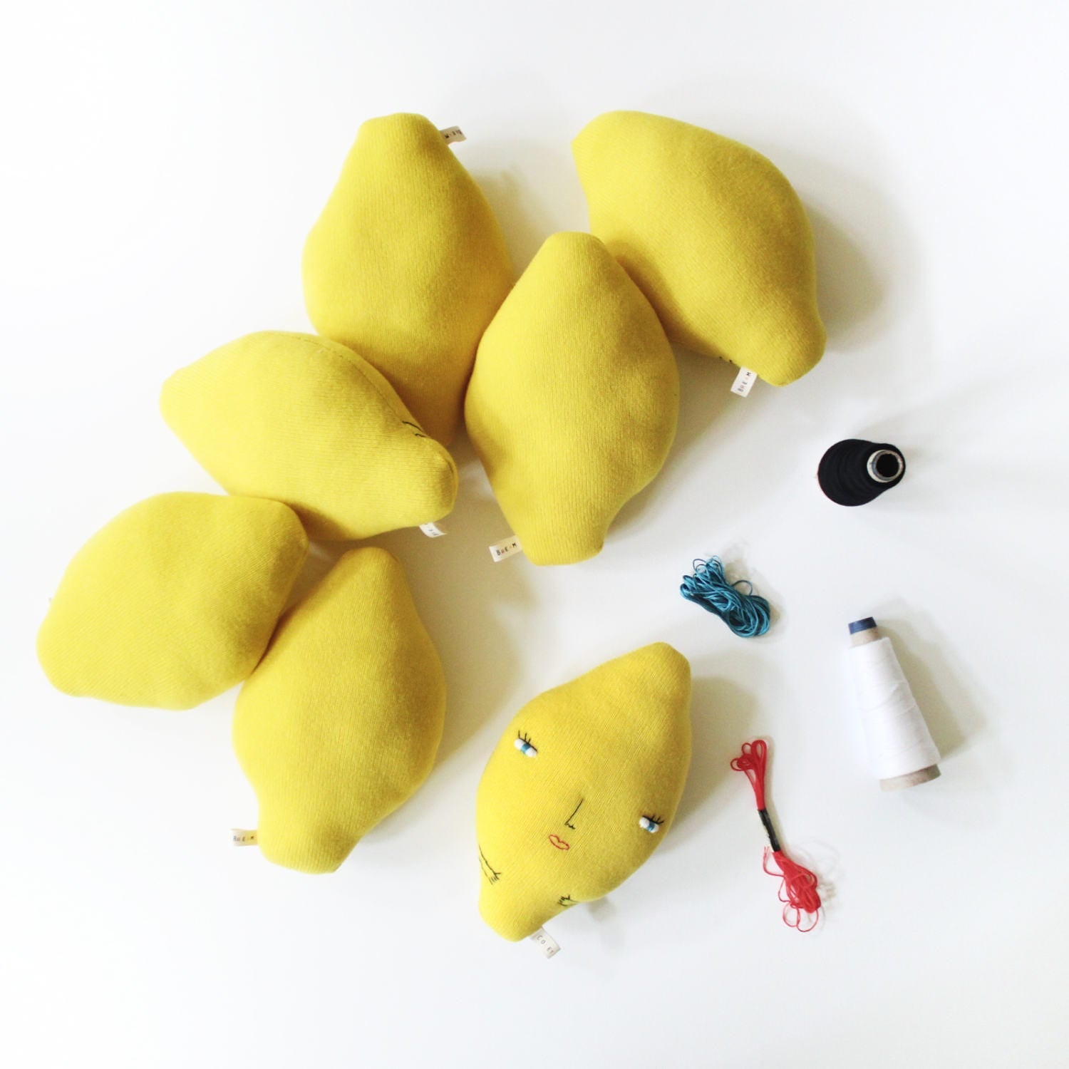 Yellow lemon-shaped cushions with face details on a white background, surrounded by sewing supplies.