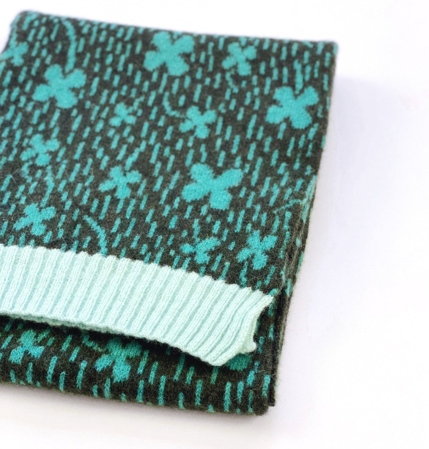 Folded knit scarf with teal shamrock pattern on a white background