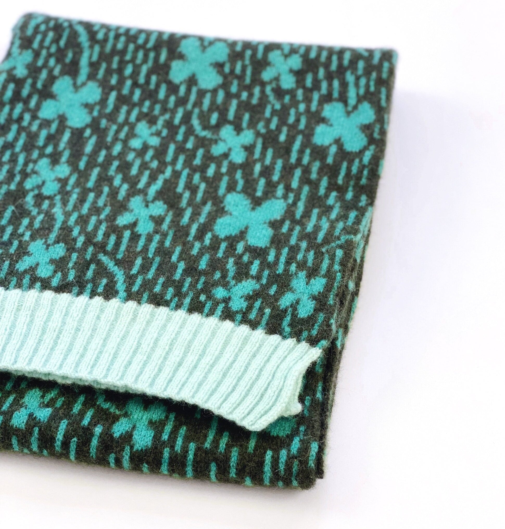 Folded knit scarf with teal shamrock pattern on a white background
