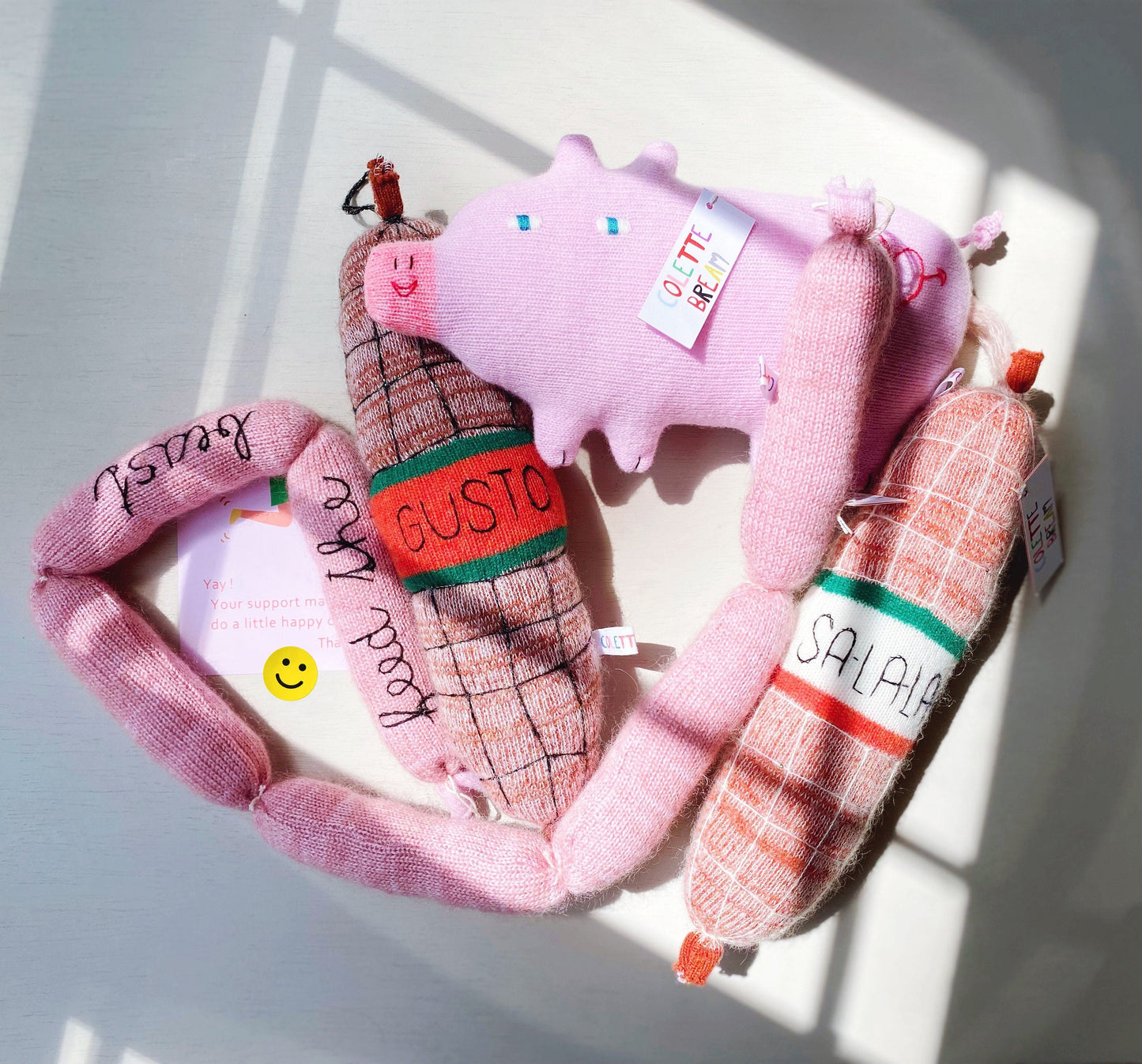 Three plush toys shaped like a pig, a sausage, and a salami on a white surface.