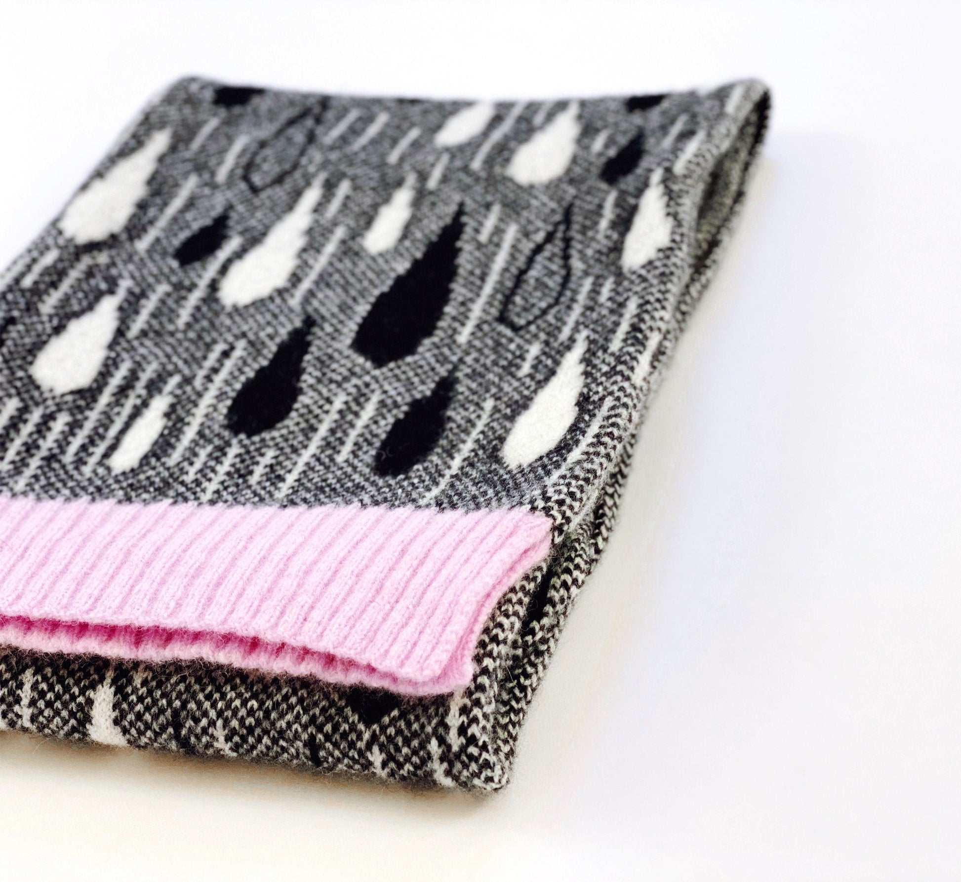 Folded knitted scarf with black and white raindrop pattern and pink trim on a white background