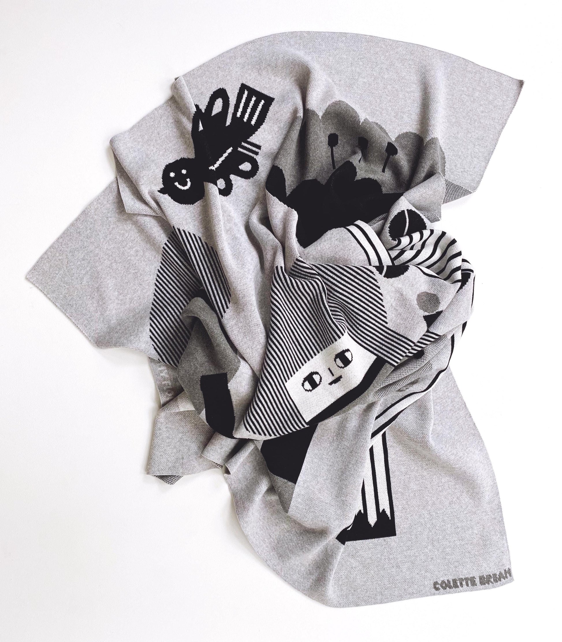 Gray knitted blanket with black and white abstract designs on a white background