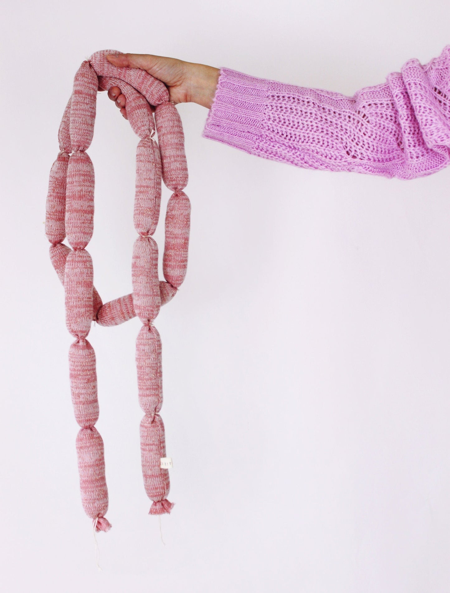Pink knitted sausagelinks held by a person against a white background