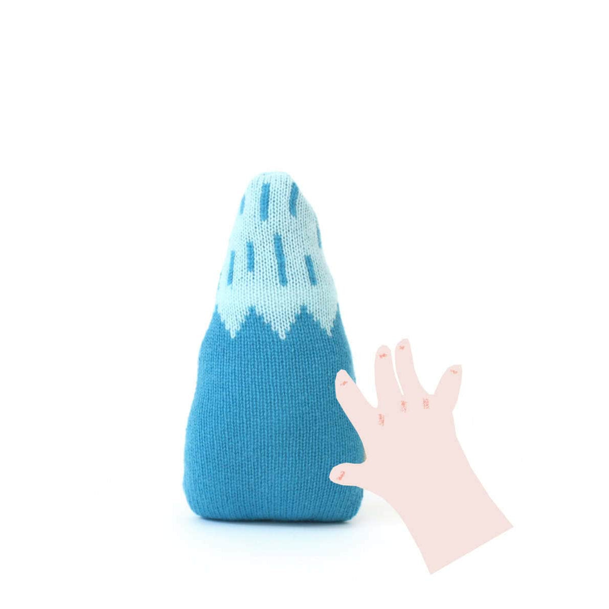 Blue and white knitted mountain baby rattle toy with a hand reaching towards it on a white background