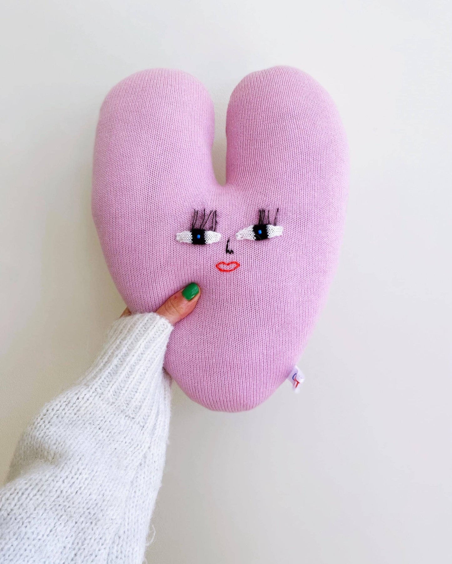 Heart-shaped knitted pillow cushion with face design held by a person against a white background