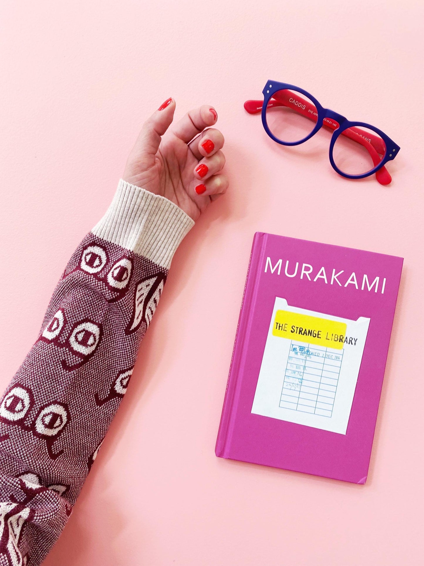 Pink book on a pink background with a hand and glasses.