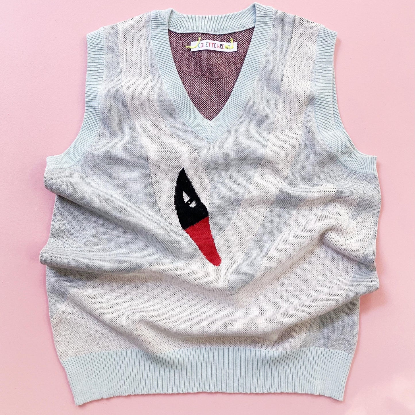 Light blue sweater vest with a white swan motif design on a pink background