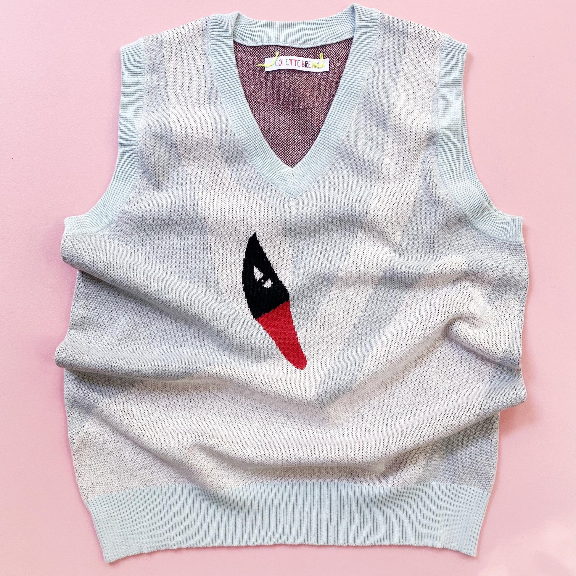 Light blue sweater vest with a white swan motif design on a pink background