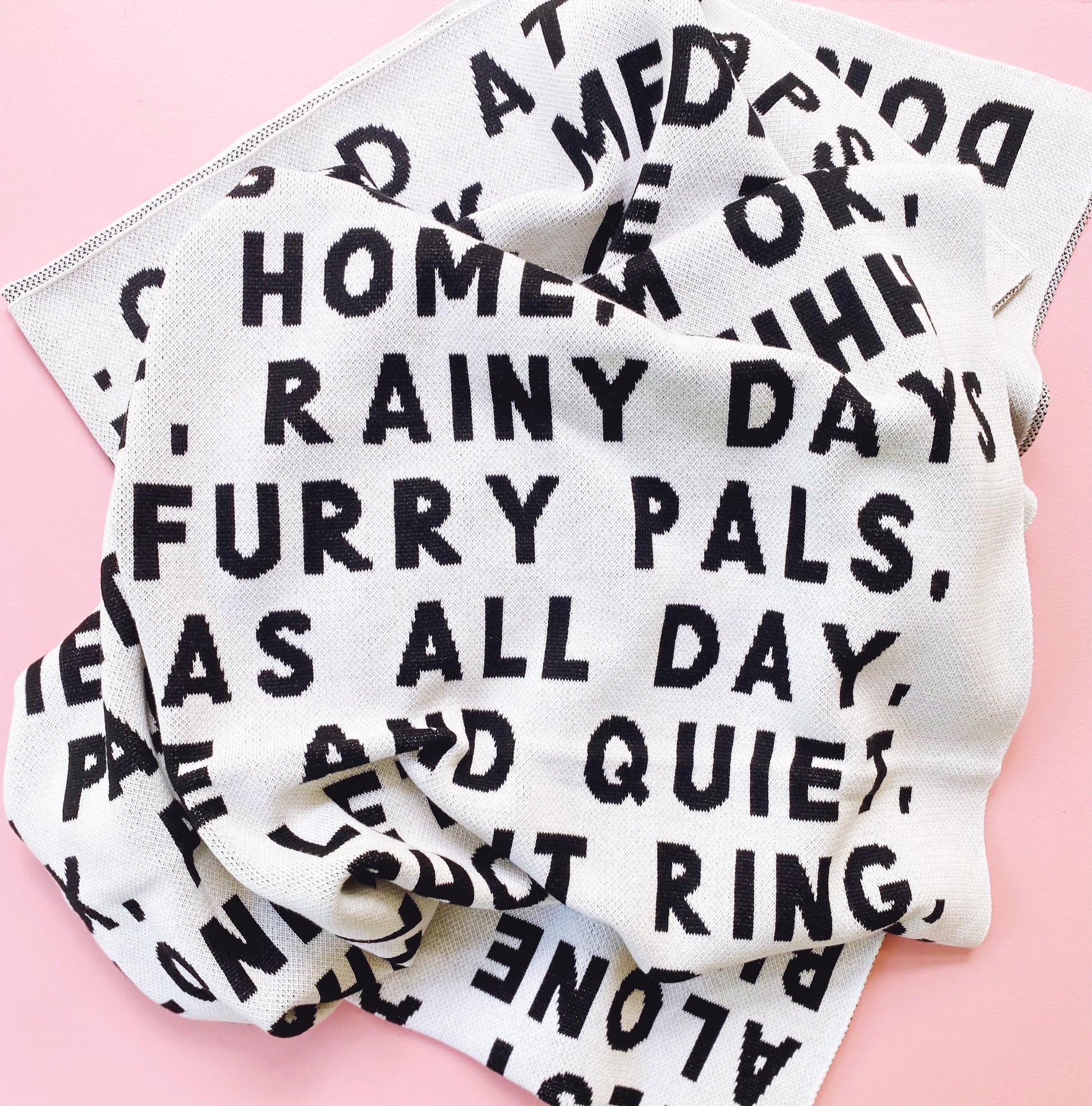 Knitted blanket throw with black and white text on a pink background