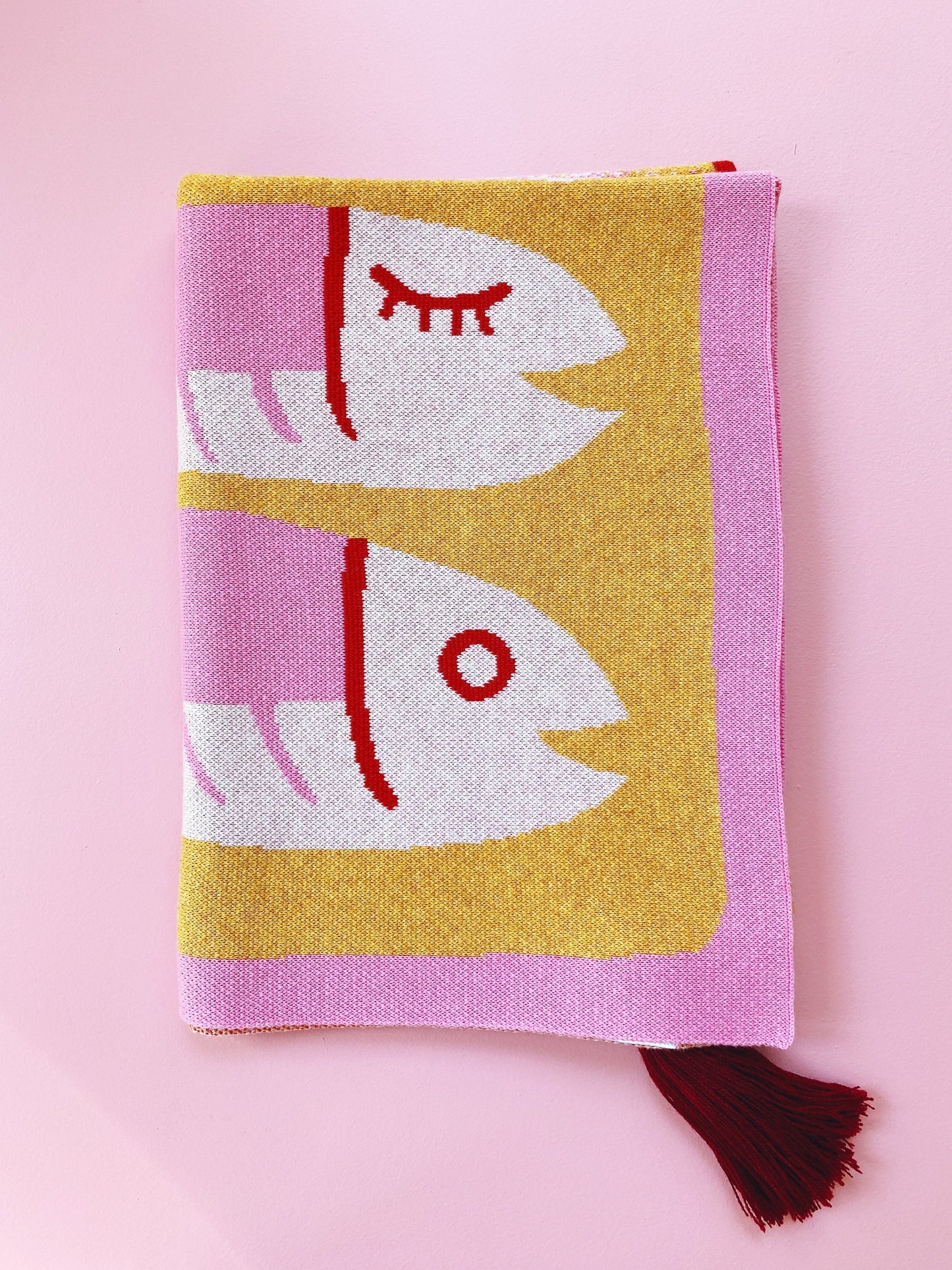 Folded knit blanket fabric with a sardines fish design on a pink background