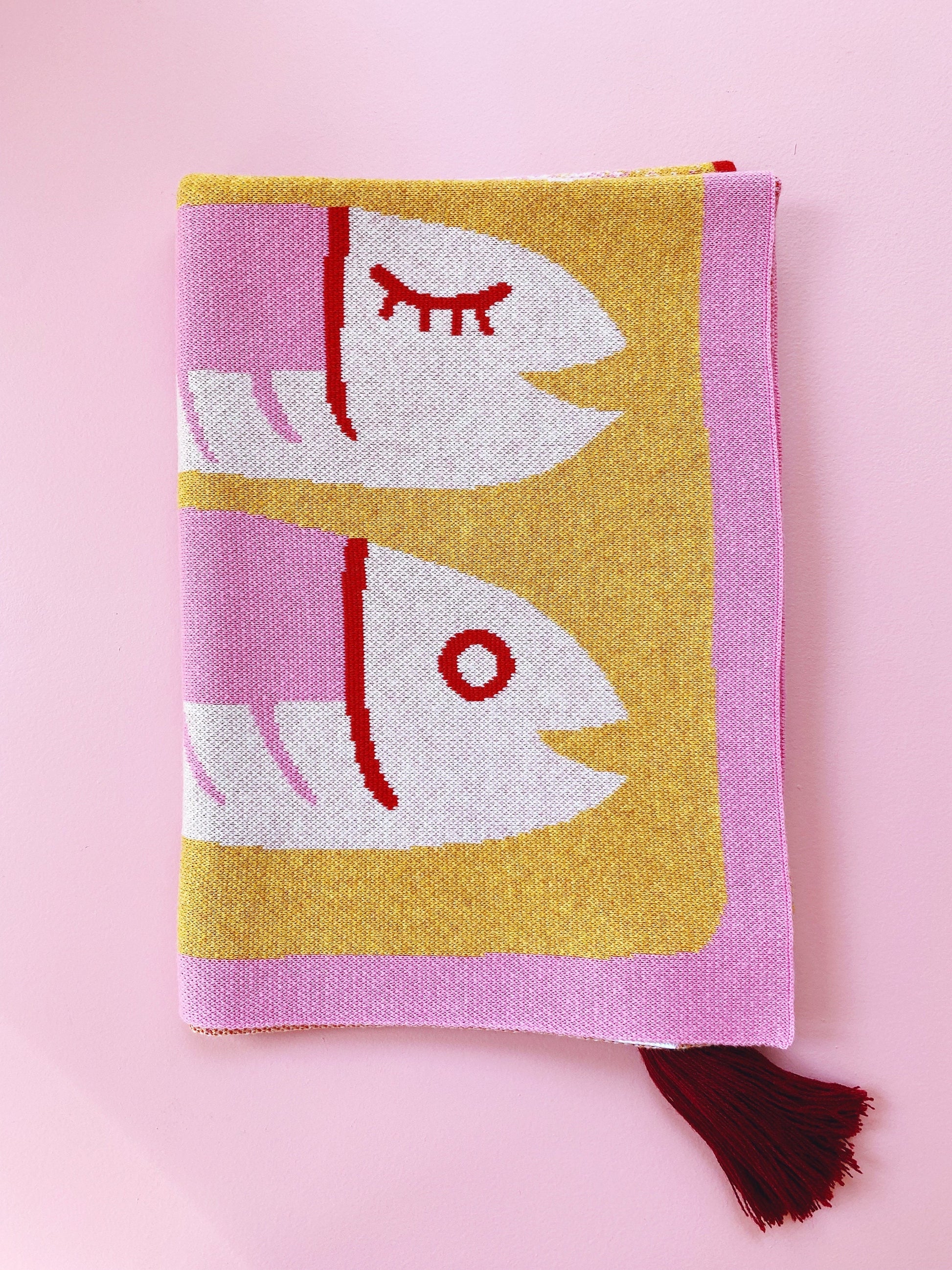 Folded knit blanket fabric with a sardines fish design on a pink background