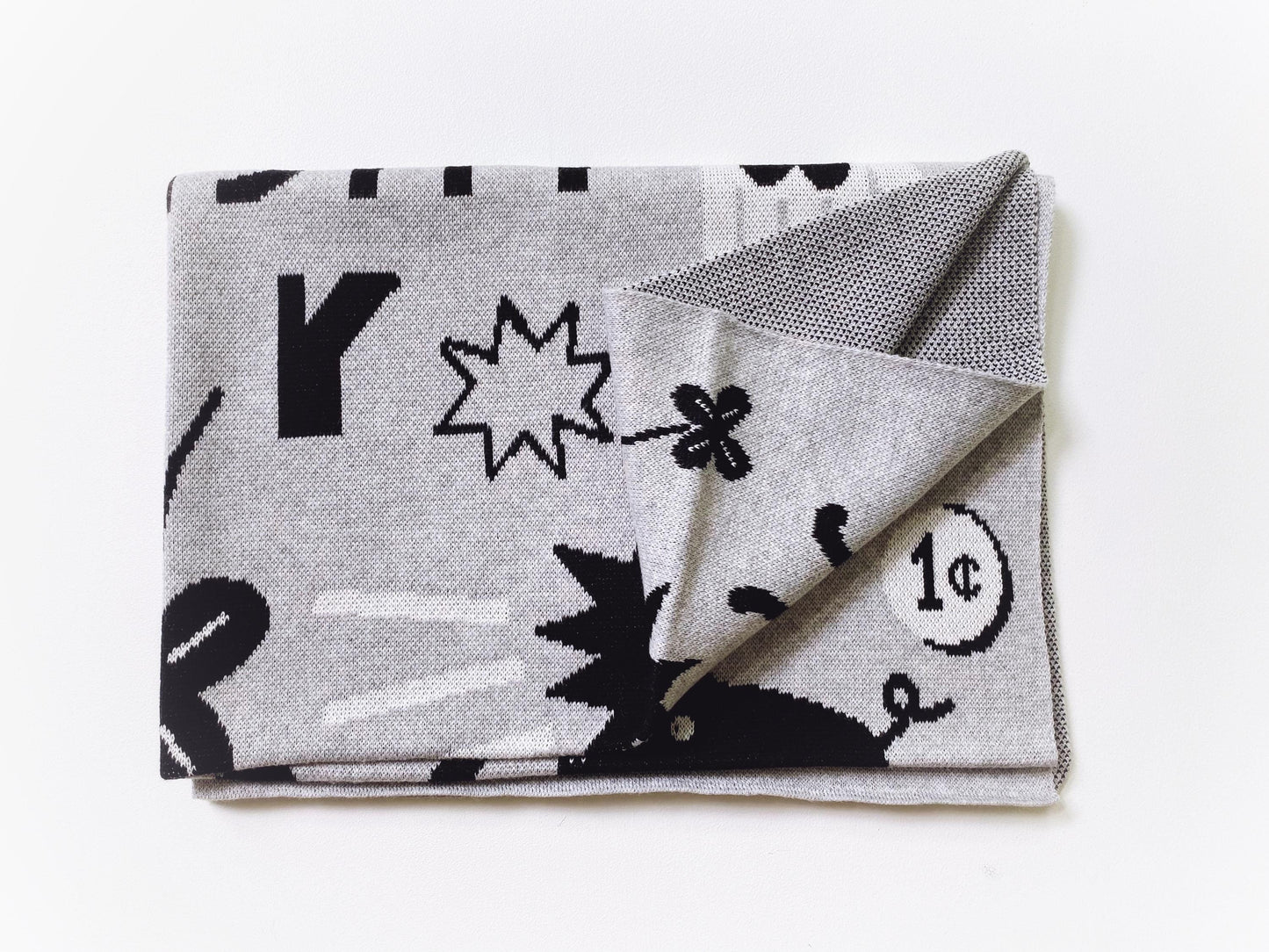 Folded knit baby blanket with black and white good luck sumbols pattern on a white background