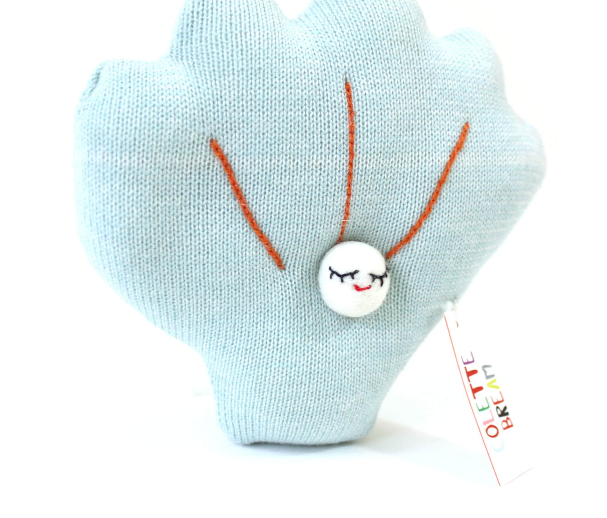 Light blue shell-shaped knitted plush toy with a smiling face and orange details on a white background