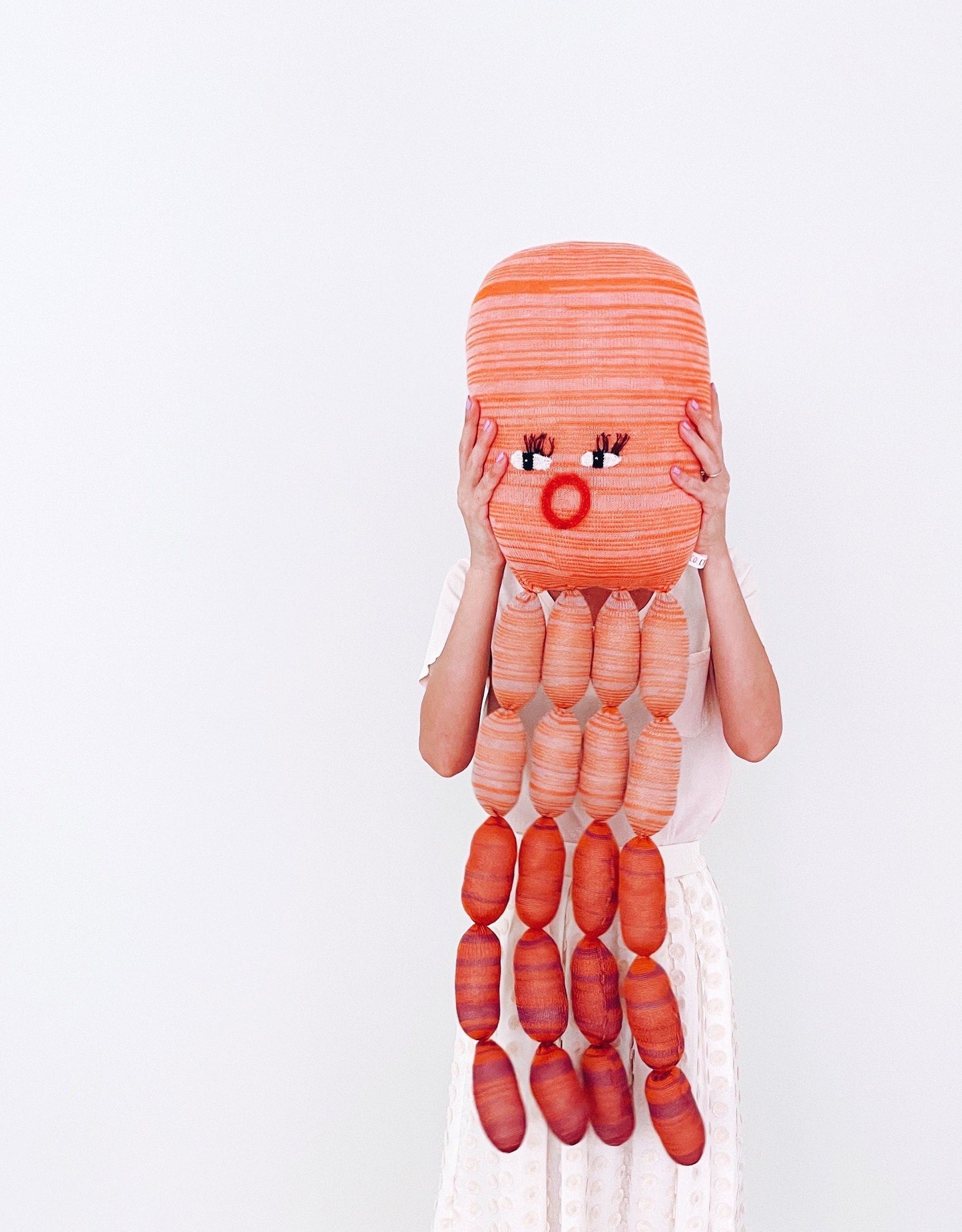 Person holding a giant orange octopus knitted toy plush on a white background