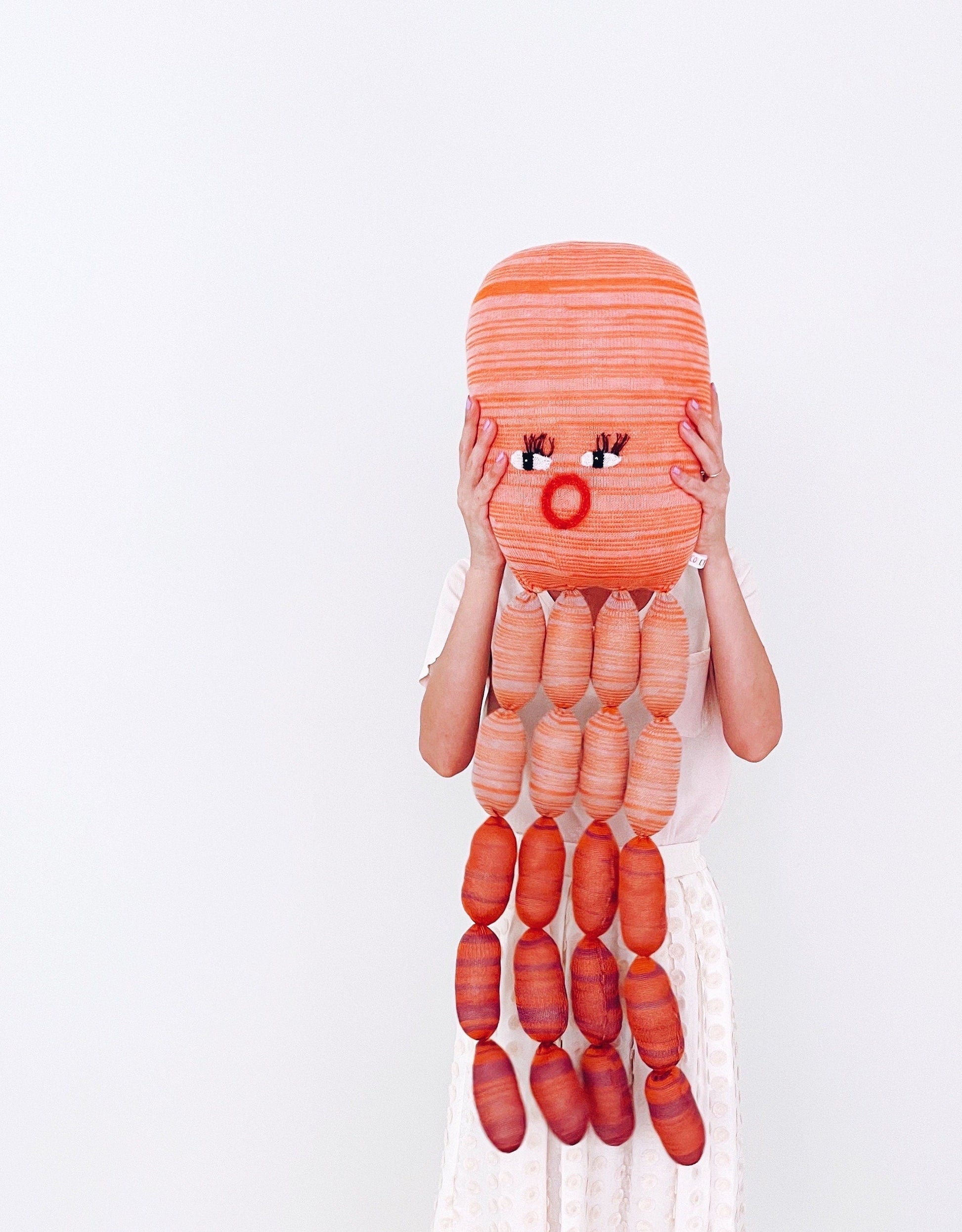 Person holding a giant orange octopus knitted toy plush on a white background