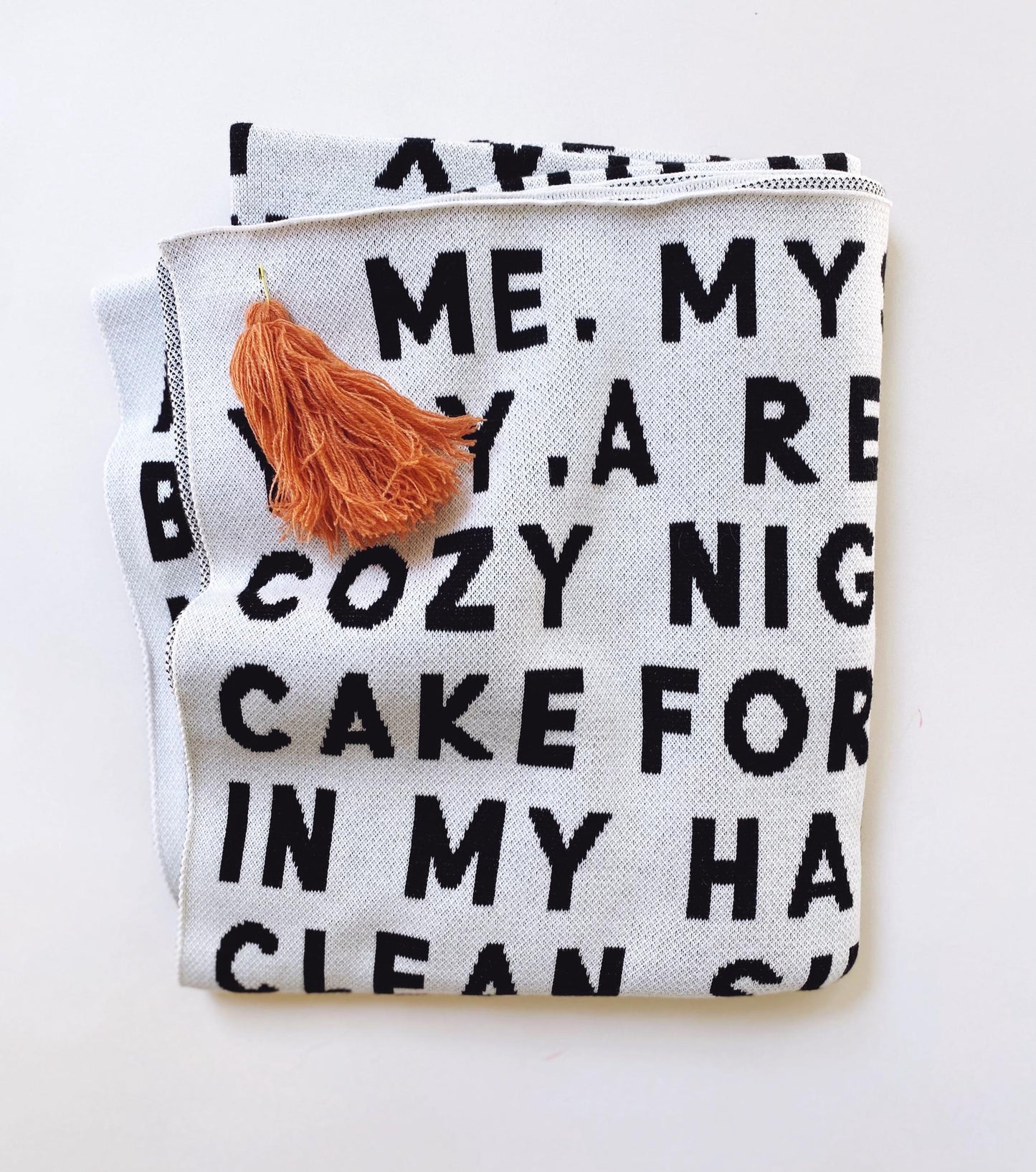Folded knit blanket throw with text and a tassel on a white background