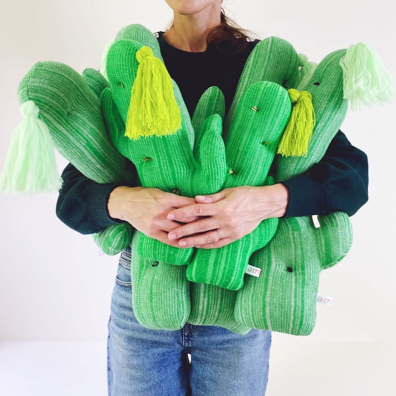 Person holding a green cactus-shaped pillows with tassels on a white background
