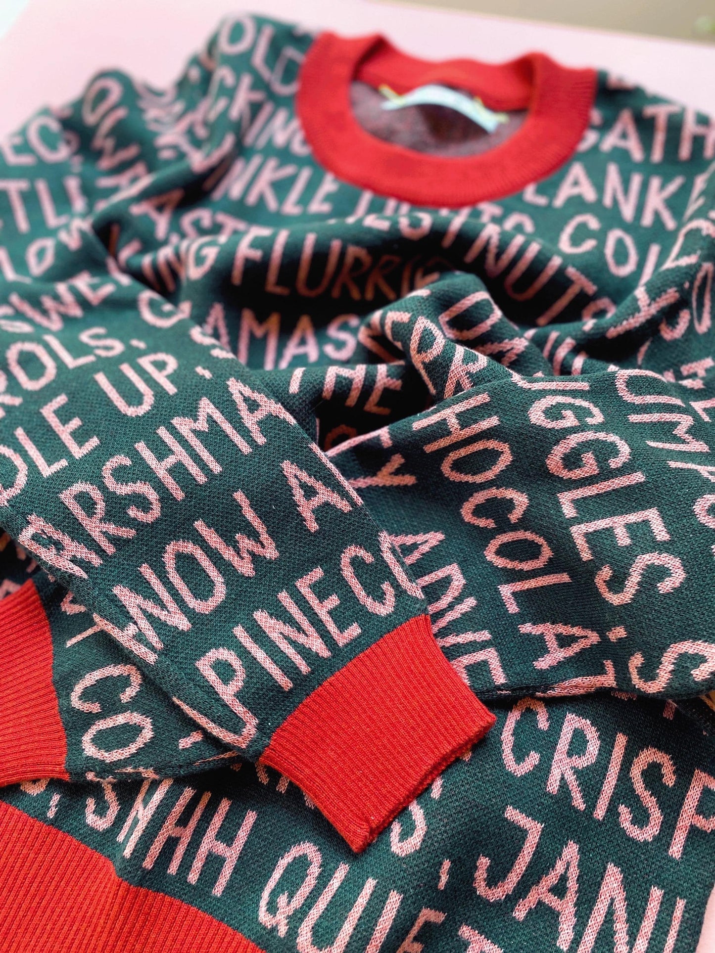 Knitted holiday sweater with festive christmas text pattern on a pink surface