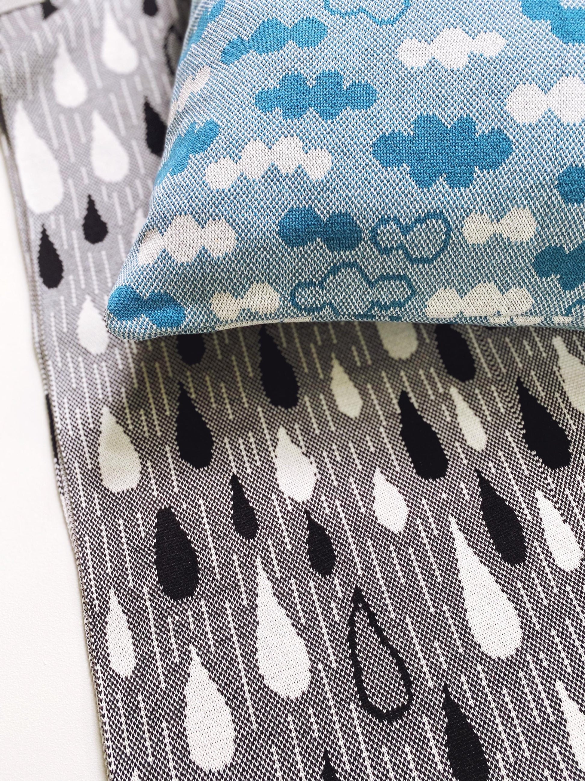 Close-up of knit fabric with raindrop pattern and a blue knit pillow with cloud pattern.