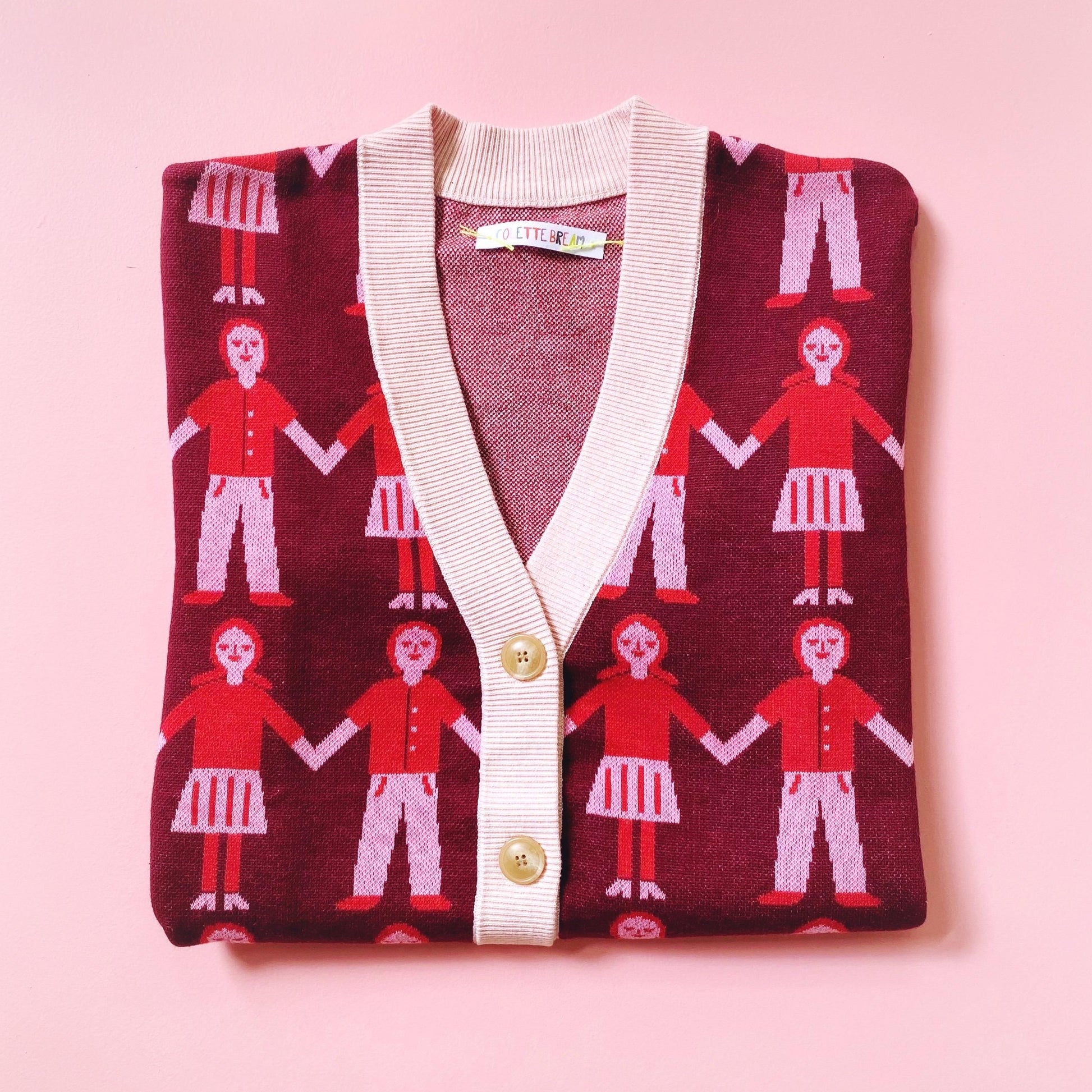 Knit sweater cardigan with a pattern of people holding hands on a pink background