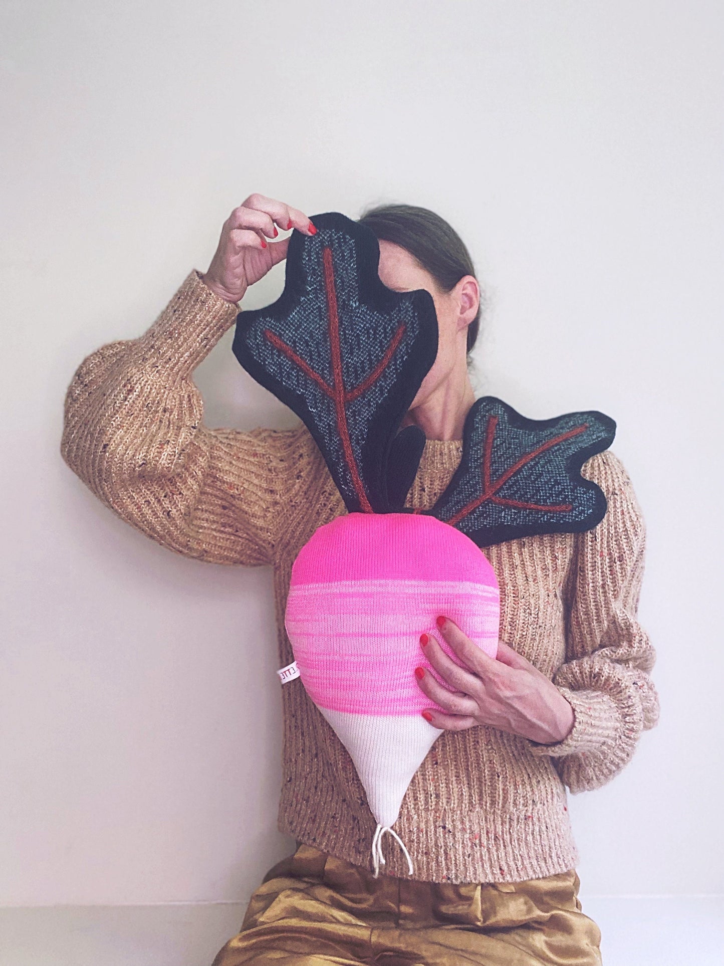 Person holding a pink decorative pillow resembling a radish with leaves against a white background