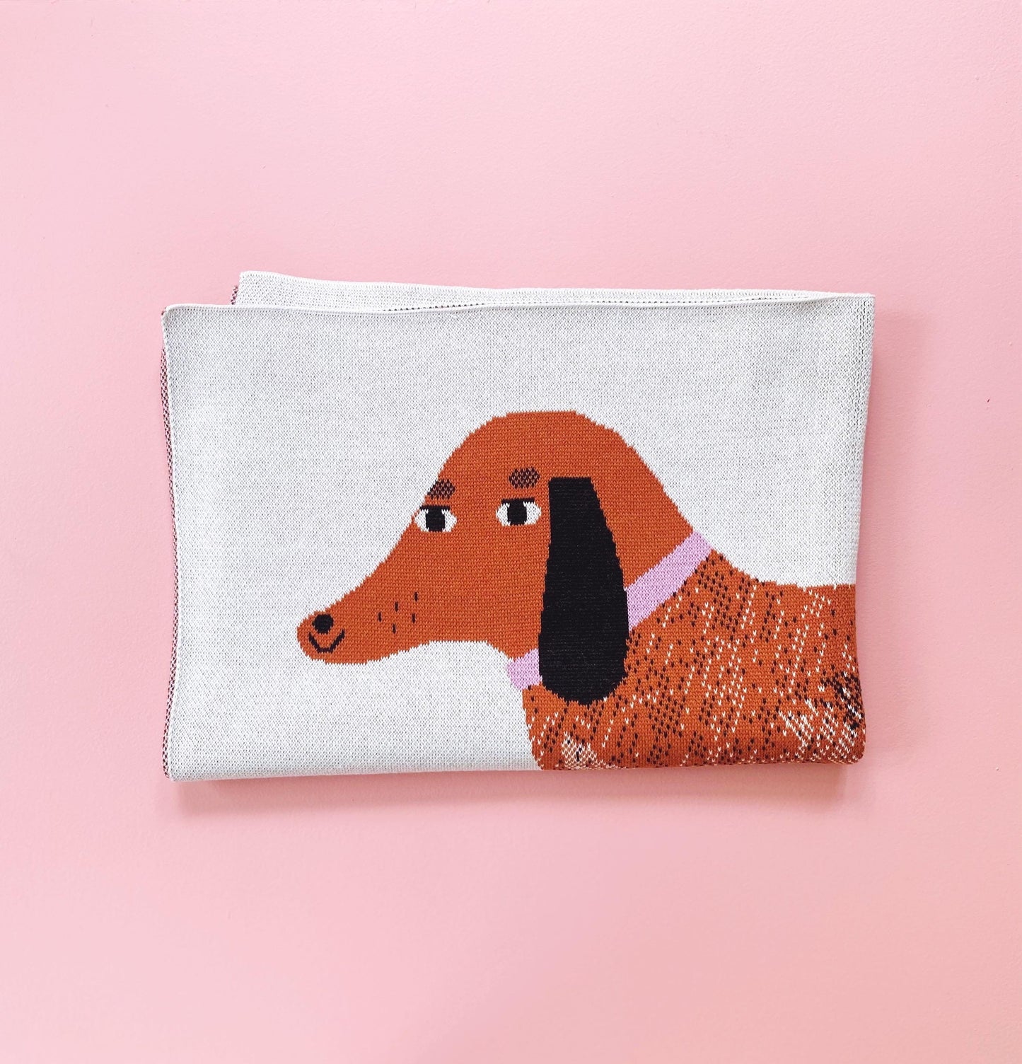 Brown dachshund design on a folded knit blanket against a pink background