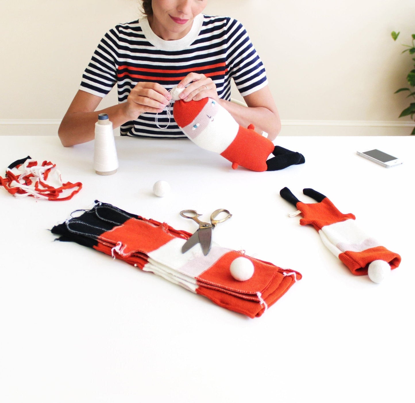 Person sewing a red and white Santa toys on a table with sewing supplies.