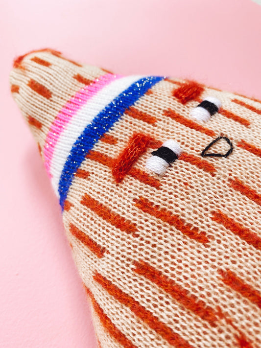 Soft knitted lambswool coconut plush toy with embroidered design on a pink background