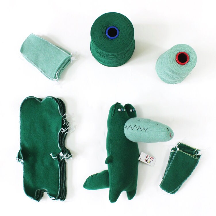 Green knitted plush toy alligator crocodile with sewing materials on a white background