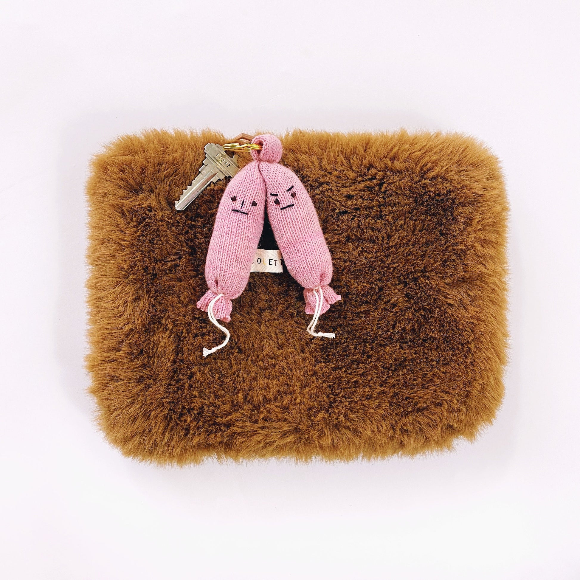 Brown fluffy pouch with a pink knitted sausage keychain on a white background