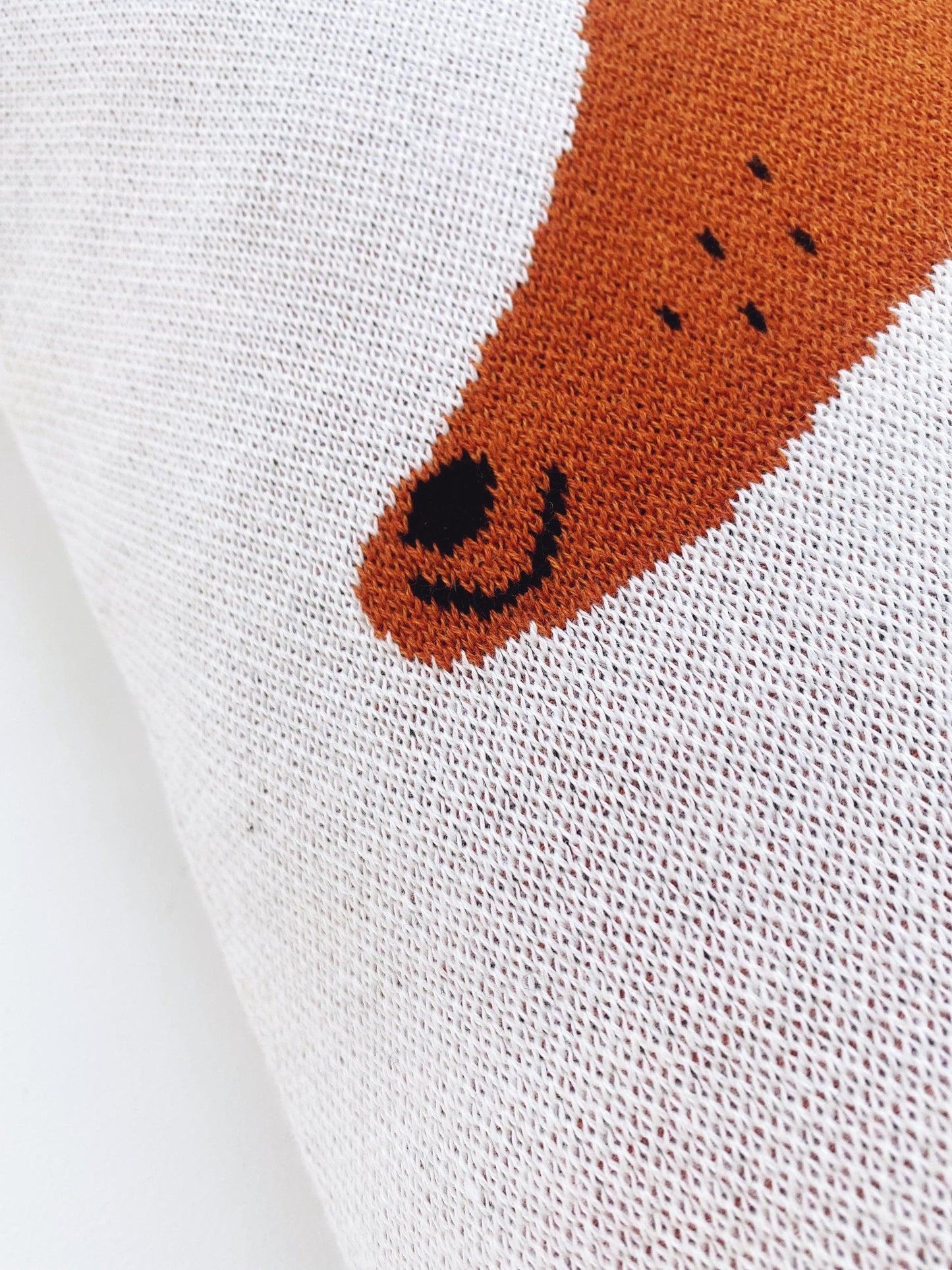 Close-up of a knitted fabric pillow with a brown dachshund face design. 