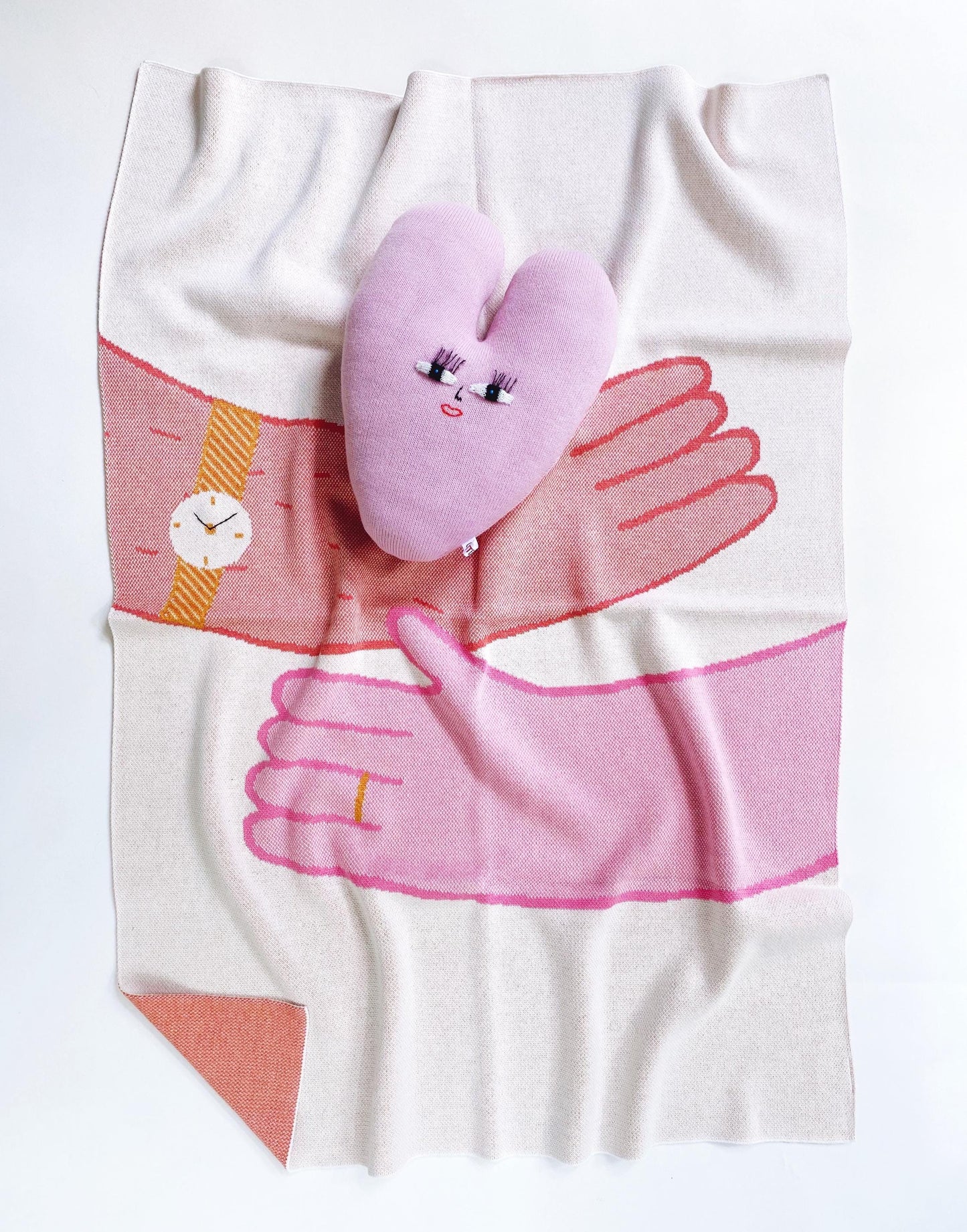 Blanket with a design of hands hugging holding a heart shaped pillow with a face on it 